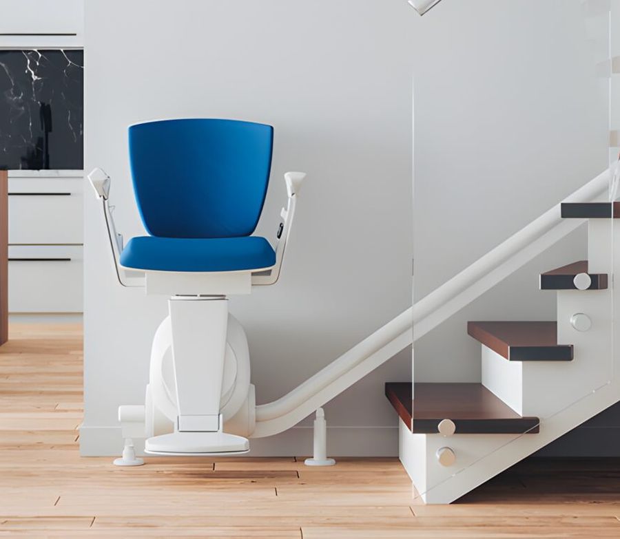 A stairlift seat parked at the foot of a curved staircase, with its rail fixed along the treads